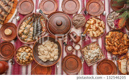 Traditional Ukrainian Christmas Eve dinner table with kutia, varenyky, stuffed cabbage rolls, fried fish, festive dishes served in bowls on embroidered rushnyk, authentic Sviat Vechir meal top view Traditional Ukrainian Christmas Eve dinner table with kutia, varenyky, stuffed cabbage rolls, fried fish, festive dishes served in bowls on embroidered rushnyk, authentic Sviat Vechir meal top view 132546205