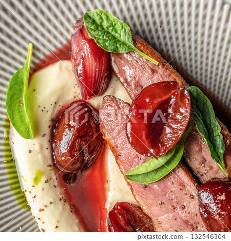 Gourmet duck breast served with creamy mashed potatoes, caramelized onions, cherry sauce, and fresh spinach leaves, plated elegantly in close-up view. 132546304