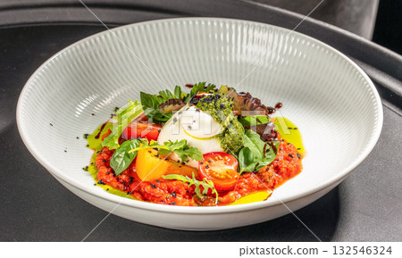 Italian burrata cheese served with tomato concasse, pesto sauce, and fresh basil on a white plate 132546324