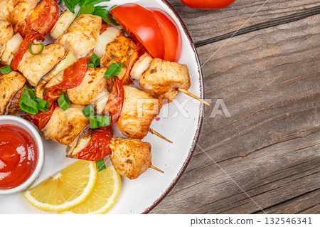 Grilled chicken skewers with roasted vegetables, tomato, onion, lemon slices and ketchup. Traditional barbecue dish served on a rustic wooden table 132546341
