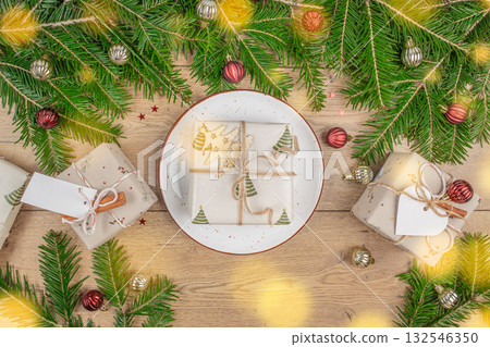 Christmas composition with gift box on a plate surrounded by fir branches and festive decorations on wooden table, holiday background with copy space for celebration Christmas composition with gift box on a plate surrounded by fir branches and festive decorations on wooden table, holiday background with copy space for celebration 132546350