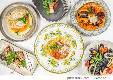 Top view of assorted Italian gourmet dishes including spaghetti with tomato sauce, seafood risotto, black pasta with shrimp and mussels, eggplant rolls, and breaded chicken cutlet 132546390
