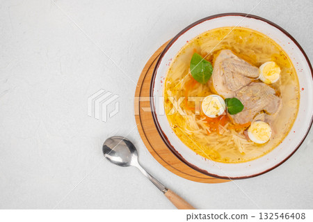 Homemade quail soup with noodles, quail meat, boiled quail eggs, and vegetables served in a white bowl with spoon on light background. top view. copy space Homemade quail soup with noodles, quail meat, boiled quail eggs, and vegetables served in a white bowl with spoon on light background. top view. copy space 132546408