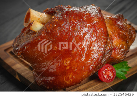roasted pork knuckle with crispy glazed skin, served with cherry tomato and parsley on a wooden board roasted pork knuckle with crispy glazed skin, served with cherry tomato and parsley on a wooden board 132546429