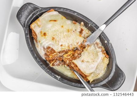 Traditional Italian lasagna with layers of pasta, rich meat sauce, and creamy melted cheese, served in a black baking dish on a white plate. 132546443