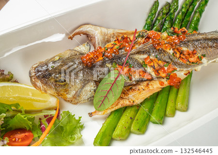 Whole grilled seabass served with asparagus, salmon roe, lemon, and fresh salad garnish 132546445