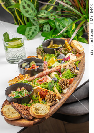 A large wooden board filled with assorted appetizers, vegetables, bread, and dips served with a cocktail A large wooden board filled with assorted appetizers, vegetables, bread, and dips served with a cocktail 132546448