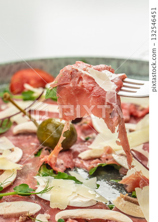 Close-up of beef carpaccio with parmesan shavings, mushrooms, greens, and a caper berry on a plate 132546451