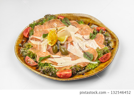 Plate of salmon carpaccio served with parmesan shavings, capers, lemon, tomato, and fresh greens 132546452