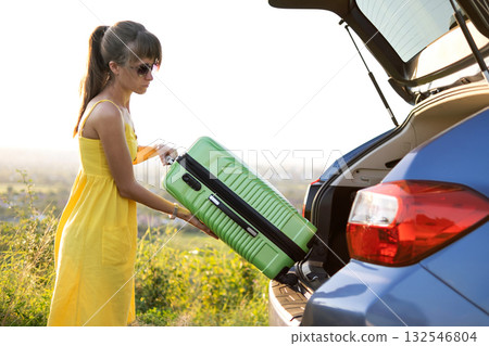 Young woman packing green suitcase in her car trunk. Travel and vacations concept. Young woman packing green suitcase in her car trunk. Travel and vacations concept. 132546804