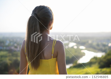 Young woman in summer dress standing outdoors enjoying warm day. Young woman in summer dress standing outdoors enjoying warm day. 132546805