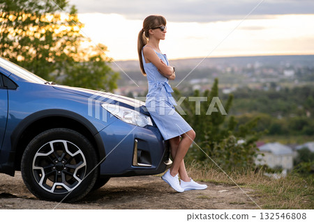 Young woman driver enjoying warm summer day standing beside her car. Travelling and vacation concept. 132546808