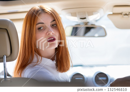 Young redhead woman driver driving a car backwards. Young redhead woman driver driving a car backwards. 132546810