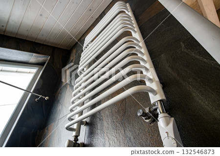 White contemporary electric towel dryer mounted on black tiled wall in modern bathroom. White contemporary electric towel dryer mounted on black tiled wall in modern bathroom. 132546873