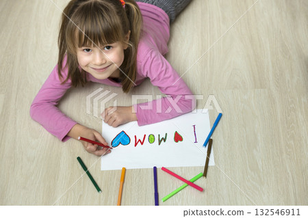 View from above of cute child girl drawing with colorful crayons I love Mom on white paper. Art education, creativity concept. View from above of cute child girl drawing with colorful crayons I love Mom on white paper. Art education, creativity concept. 132546911