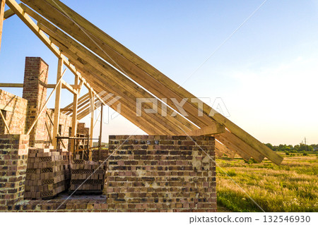 Unfinished brick house with wooden roof structure under construction. 132546930