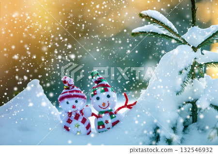 Two small funny toys baby snowman in knitted hats and scarves in deep snow outdoors near pine tree branch. Happy New Year and Merry Christmas greeting card. Two small funny toys baby snowman in knitted hats and scarves in deep snow outdoors near pine tree branch. Happy New Year and Merry Christmas greeting card. 132546932