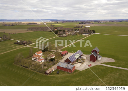 Top view of rural landscape on sunny spring day. Farm with solar photo voltaic panels system on wooden building, barn or house roof. Green field copy space background. Renewable energy production. 132546959