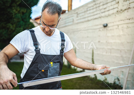 Mature male carpenter measuring wooden plank outdoors 132546981
