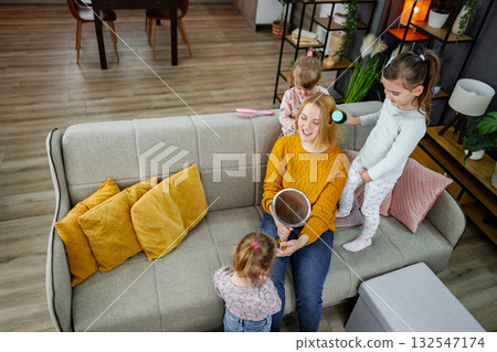 Three little girls are doing their mom's hair 132547174