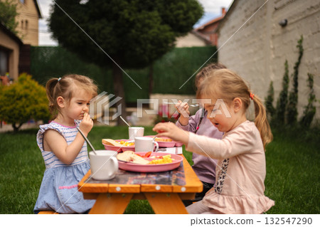 Young children enjoying a delightful outdoor meal in bright sunshine Young children enjoying a delightful outdoor meal in bright sunshine 132547290