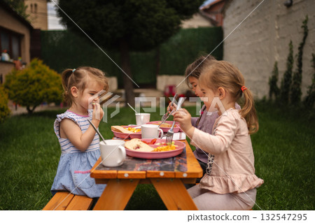 Joyful meal time for children in a sunny backyard gathering Joyful meal time for children in a sunny backyard gathering 132547295