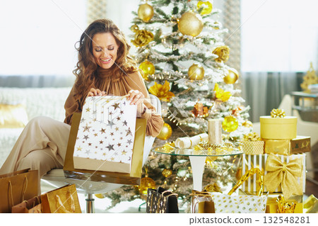 Smiling Woman Looking into Festive Shopping Bag Smiling Woman Looking into Festive Shopping Bag 132548281
