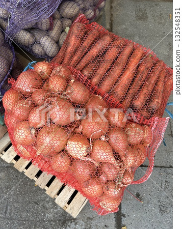 Fresh vegetables in mesh bags, featuring vibrant orange carrots and reddish onions, displayed on wooden crate at market, showcasing organic produce and healthy lifestyle 132548351