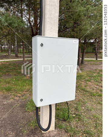 Electrical utility box mounted on a concrete pole in a green park area, surrounded by trees and grass, showcasing infrastructure in a natural environment Electrical utility box mounted on a concrete pole in a green park area, surrounded by trees and grass, showcasing infrastructure in a natural environment 132548353