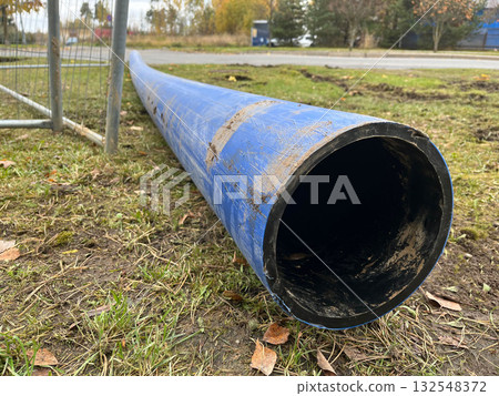Blue plastic pipe lying on the ground, surrounded by grass and dirt, showcasing construction materials and outdoor environment with natural elements 132548372