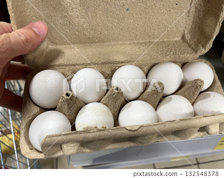 Hand holding an open carton of white eggs, showcasing ten eggs nestled in a recycled paper container, emphasizing freshness and natural food products for culinary use 132548378