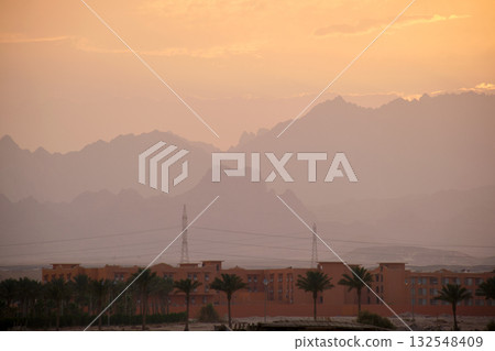 Sunset landscape with remote hotel complex against dark mountain peaks in egyptian desert Sunset landscape with remote hotel complex against dark mountain peaks in egyptian desert 132548409