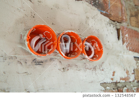 Socket orange boxes with wires in a wall. Cabling installation of electrical wires sticking out from electrical sockets hole on brick wall. 132548567