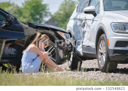 Sad female driver sitting on street side shocked after car accident. Road safety and vehicle insurance concept Sad female driver sitting on street side shocked after car accident. Road safety and vehicle insurance concept 132548621