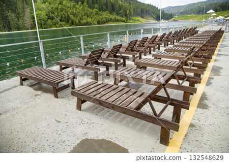 Row of empty wooden beach chairs near water. Row of empty wooden beach chairs near water. 132548629