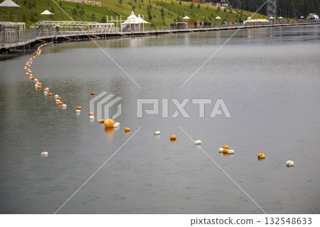 Rope with white and yellow restriction markers on water surface for prohibiting of swimming in deep lake or sea. Rope with white and yellow restriction markers on water surface for prohibiting of swimming in deep lake or sea. 132548633