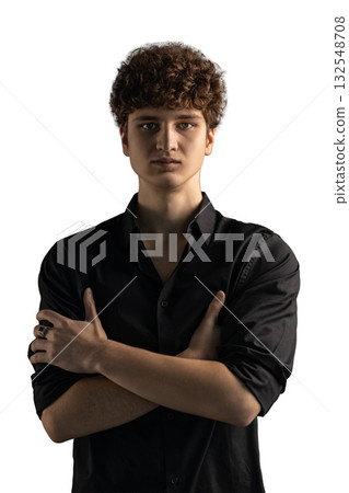 young man stands confidently with his arms crossed in front of his chest. He has curly hair and wears a simple black shirt in a well lit studio environment. young man stands confidently with his arms crossed in front of his chest. He has curly hair and wears a simple black shirt in a well lit studio environment. 132548708