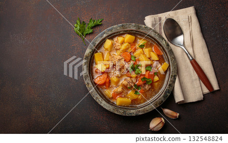 Chicken stew or soup with potatoes and carrots served in rustic bowl with spoon top view on dark brown concrete background, space for text Chicken stew or soup with potatoes and carrots served in rustic bowl with spoon top view on dark brown concrete background, space for text 132548824