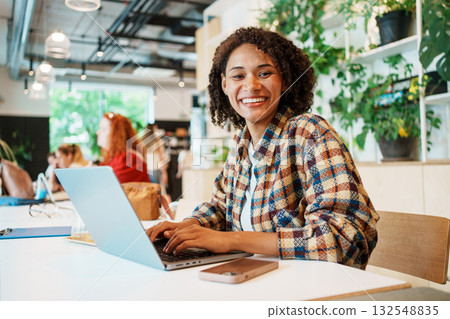 A Young Woman Engaged in Creative Work in a Modern Workspace While Using Her Laptop 132548835