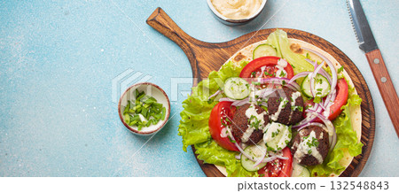 Preparing and cooking falafel wrap on pita on wooden cutting board with hummus top view light blue background, space for text Preparing and cooking falafel wrap on pita on wooden cutting board with hummus top view light blue background, space for text 132548843