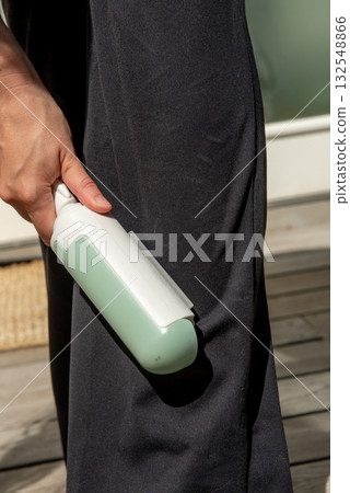 Woman using reusable clothes lint roller cleaner. Close up of woman removing dog hair from clothing 132548866