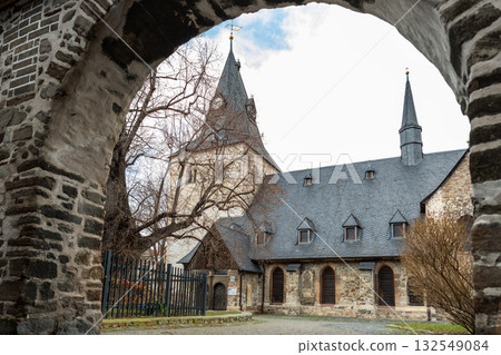 View of Neue Evangelische Kirchengemeinde in Wernigerode Germany through ancient stone archway. Elegant slate spires and historic stone walls radiate calm dignity and enduring faith View of Neue Evangelische Kirchengemeinde in Wernigerode Germany through ancient stone archway. Elegant slate spires and historic stone walls radiate calm dignity and enduring faith 132549084