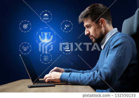 Professional using laptop in modern workspace with digital law icons surrounding him Professional using laptop in modern workspace with digital law icons surrounding him 132550133