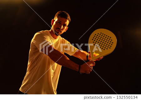 Man practicing paddle tennis with a strong stance in a dark setting Man practicing paddle tennis with a strong stance in a dark setting 132550134