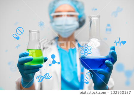 Scientist holding green and blue chemical solutions in a laboratory during the day 132550187