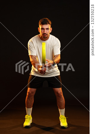Man preparing to strike with a racket in a dark studio setting, highlighting athletic focus 132550218