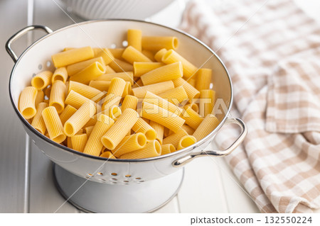 Uncooked rigatoni pasta in colander on white table. Uncooked rigatoni pasta in colander on white table. 132550224