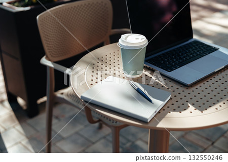 Working on a laptop with coffee at an outdoor table in a sunny cafe setting 132550246