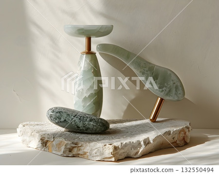 Minimal beauty setup featuring a polished jade gua-sha board, facial roller on a gold stand, oval massage stone and jade wand arranged on a textured stone tray. Clean light and marble veins emphasize Minimal beauty setup featuring a polished jade gua-sha board, facial roller on a gold stand, oval massage stone and jade wand arranged on a textured stone tray. Clean light and marble veins emphasize 132550494