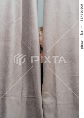 Narrow vertical slice shows a childs eye peeking between gray curtains intimate, mysterious home detail 132550506